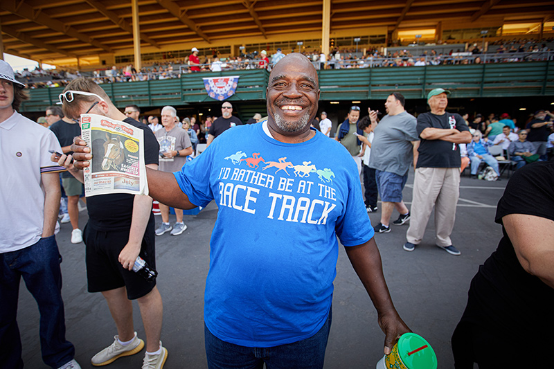 happy man at race track with shirt that says "I'd rather be at the racetrack"